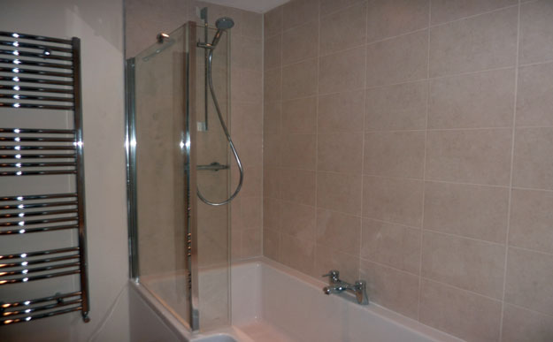 Bathroom with beige wall tiles chrome towel radiator and bath shower screen
